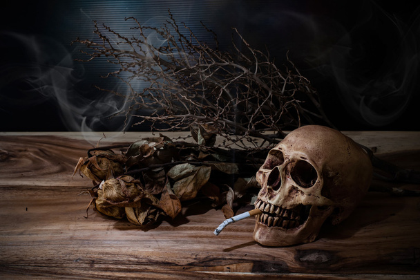 Natureza morta Fumar crânio humano com cigarro na mesa de madeira, p
 - Foto, Imagem