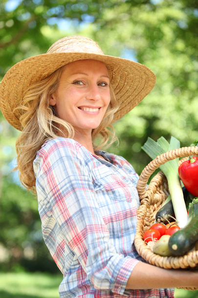 Woman smiling with a straw hat holding basket of vegetables. - Zdjęcie, obraz