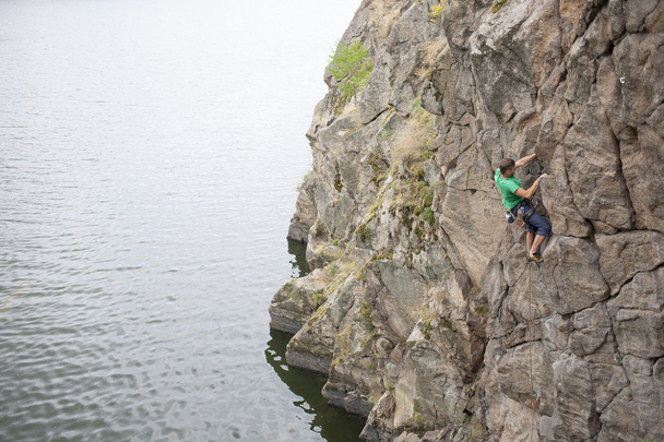Un hombre sube a la roca cerca del agua
. - Foto, Imagen