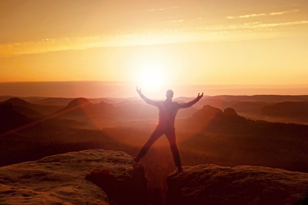 Jumping hiker in black celebrate triumph between two rocky peaks. Wonderful daybreak with sun above head.. - Photo, Image