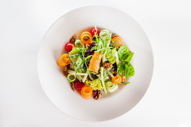 Isolated Delicios Salad with salmon, mix lettuce, arugula, cucumber, walnuts, cherry tomatoes garnished with a sprig of basil on a white plate - 写真・画像