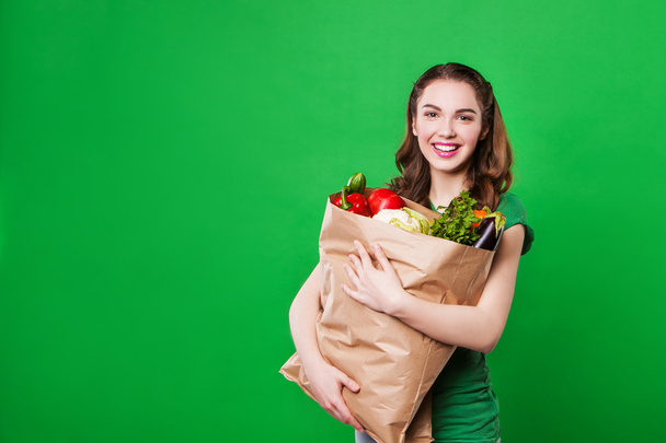 bela mulher segurando um saco de supermercado cheio de alimentos frescos e saudáveis no fundo verde
 - Foto, Imagem