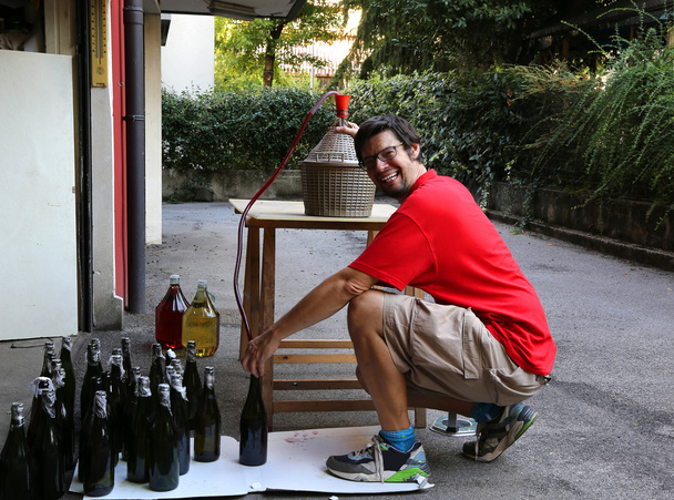 młody człowiek uśmiechający się podczas butelkowania wina w domu - Zdjęcie, obraz