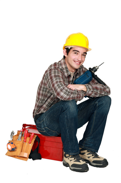 Young craftsman holding a drill and sitting on a tool box - Photo, Image