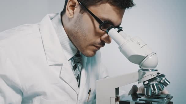 Νέος γιατρός, κοιτάζοντας μέσα από το μικροσκόπιο - Πλάνα, βίντεο