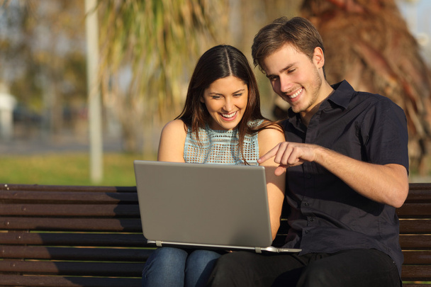 Couple watching media in a laptop sitting on a bench - Foto, imagen