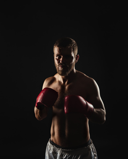 Athletic bearded boxer with gloves on a dark background - Foto, afbeelding