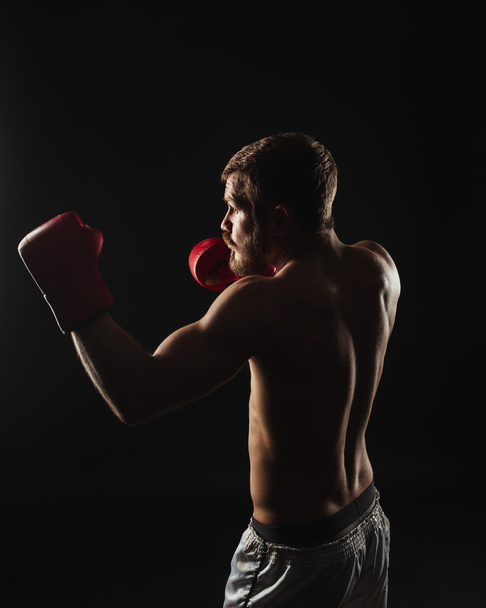 Athletic bearded boxer with gloves on a dark background - Foto, Imagen
