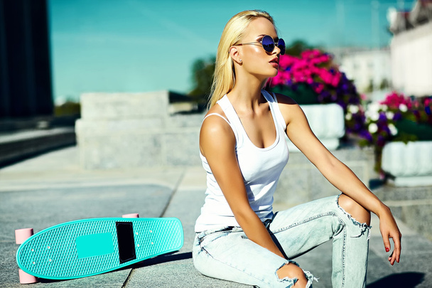 High fashion look.glamor stylish sexy beautiful young blond  model girl in summer bright casual hipster clothes with skateboard sitting in the street - Fotó, kép