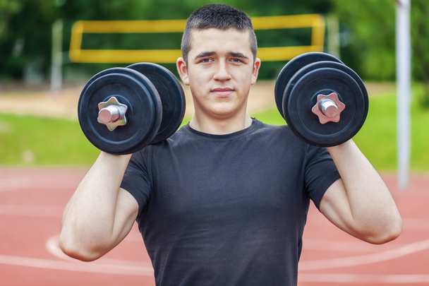 Teenager with dumbbells on sports ground - Foto, afbeelding