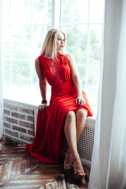 young sexy blonde woman with red lips in red dress posing in interior - 写真・画像