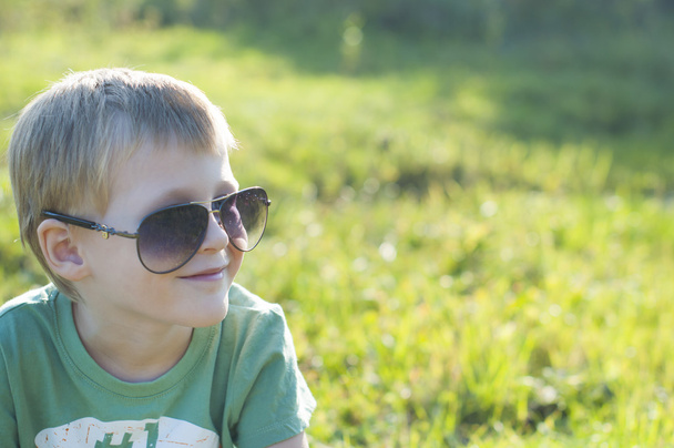 Cute adorable child in sunglasses sitting on green grass in the - Fotografie, Obrázek
