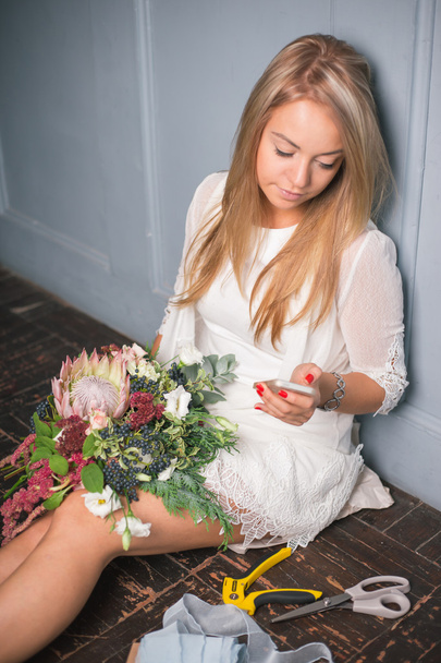 Florist at work: pretty young blond woman making fashion modern bouquet of different flowers - Photo, Image