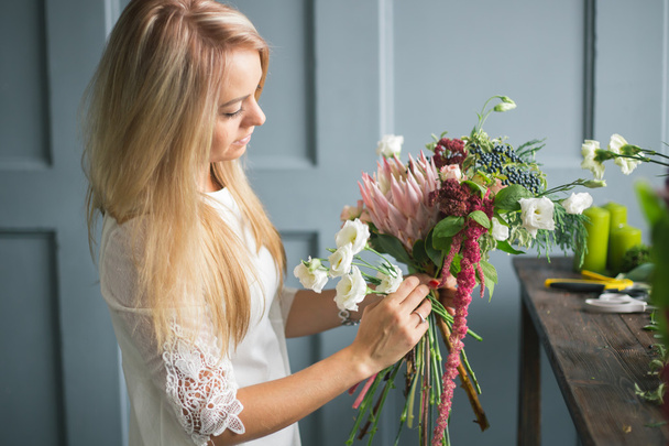Florist at work: pretty young blond woman making fashion modern bouquet of different flowers - Фото, изображение