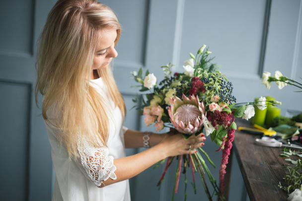 Florist at work: pretty young blond woman making fashion modern bouquet of different flowers - Foto, Imagem