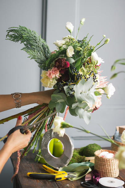 Florist at work: pretty young blond woman making fashion modern bouquet of different flowers - Foto, imagen