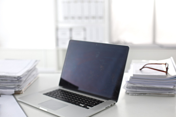 Laptop with stack of folders on table on white background - Photo, Image