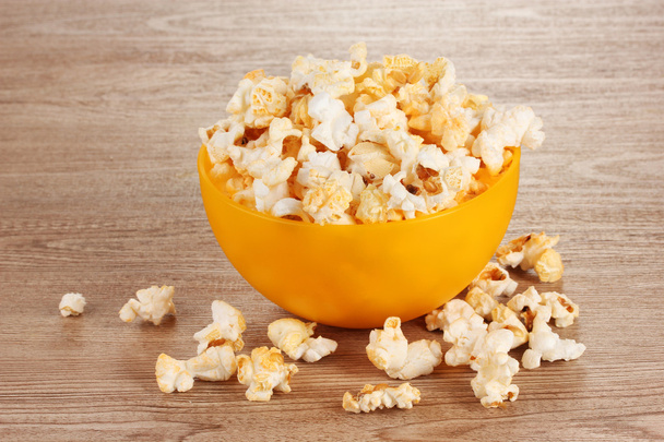 Popcorn in bright plastic bowl on wooden table - Fotografie, Obrázek