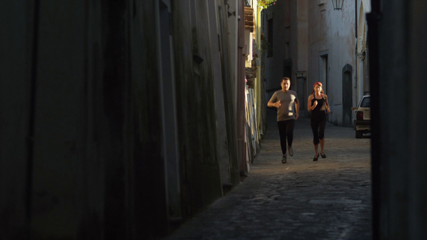 Couple jogging in narrow street - Záběry, video