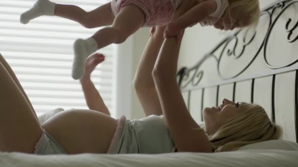 Pregnant mother playing with children on bed - Materiał filmowy, wideo