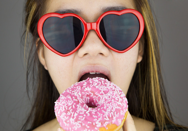 Сексуальна жінка з червоними льодяними окулярами їсть пончик
 - Фото, зображення