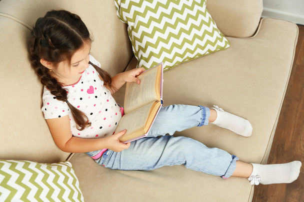 Little girl sitting on sofa with book - Zdjęcie, obraz