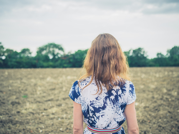 junge Frau steht an bewölktem Tag auf kargem Feld - Foto, Bild