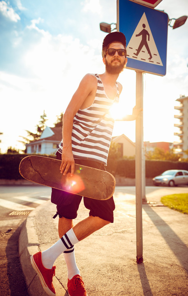 Hombre con estilo en gafas de sol con un monopatín en una calle en la c
 - Foto, imagen