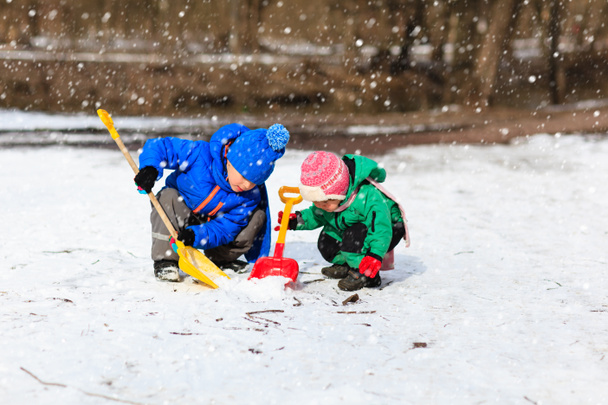 kleine jongen en meisje graven van sneeuw in de winter - Foto, afbeelding