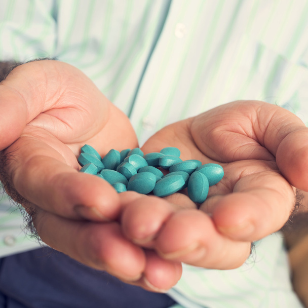 oude man met een stapel van blauwe pillen in zijn hand - Foto, afbeelding