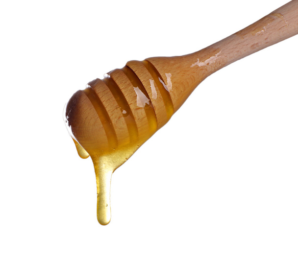 Honey dripping from a wooden honey dipper on light background - Foto, Imagen