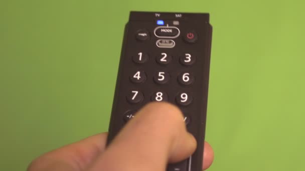 Mannenhand veranderen kanalen met afstandsbediening op een groen scherm. Frontale schot - Video