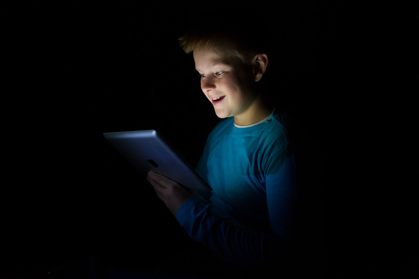 Young boy with light hair play with a tablet in dark - 写真・画像