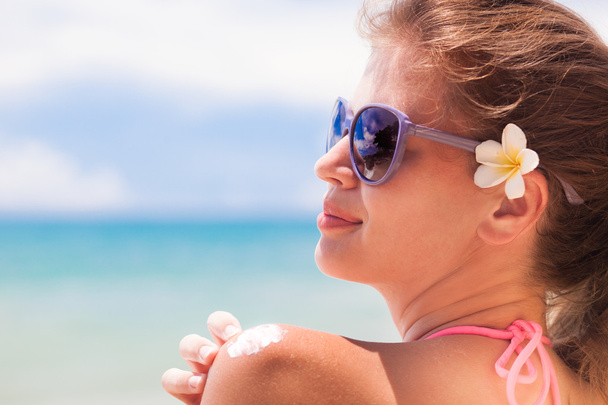 Jeune femme en lunettes de soleil mettant crème solaire sur l'épaule
 - Photo, image
