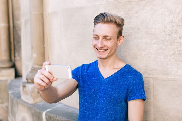 Nuori komea mies lyhyet hiukset ottaa selfie kaupunkiympäristössä mobiili
 - Valokuva, kuva