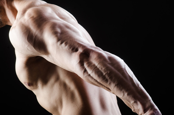 М'язистий чоловік позує в темній студії
 - Фото, зображення