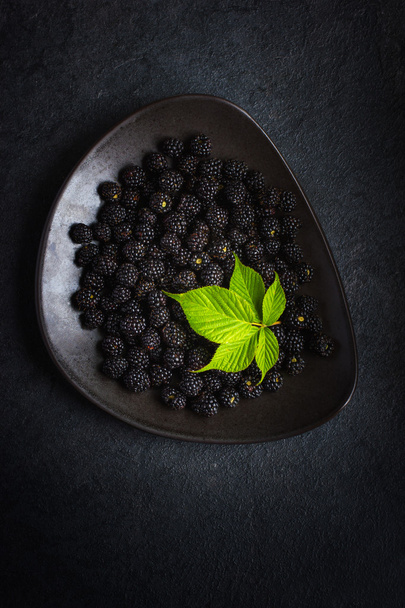 Fresh blackberry and green leaf on black plate - Photo, image
