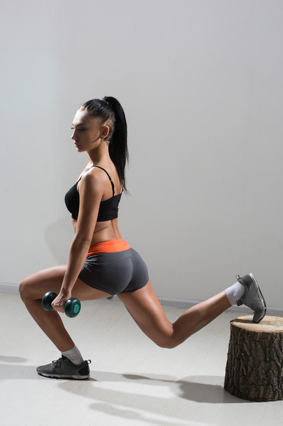 Young, beautiful, athletic girl performs squats with dumbbells in a gym. - Photo, Image