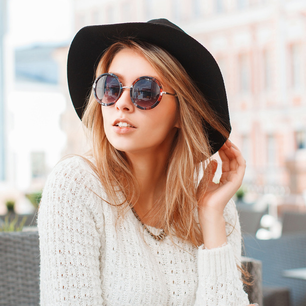 Mujer bastante de moda con sombrero negro y gafas de sol redondas en la cafetería
. - Foto, imagen