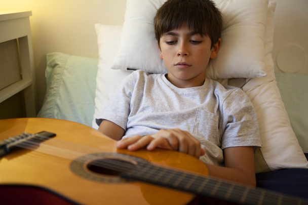 Un garçon avec une guitare espagnole dans sa chambre
 - Photo, image