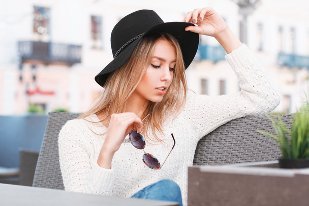 Menina elegante bonita em um chapéu e óculos de sol descansando em um dia ensolarado em um café
 - Foto, Imagem