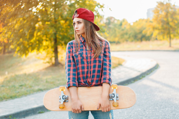 Όμορφη και μόδα νεαρή γυναίκα ποζάρουν με ένα skateboard - Φωτογραφία, εικόνα