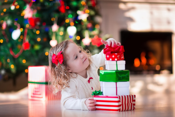 Little girl opening Christmas presents at fire place - Fotó, kép