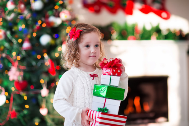 Little girl opening Christmas presents at fire place - Fotó, kép