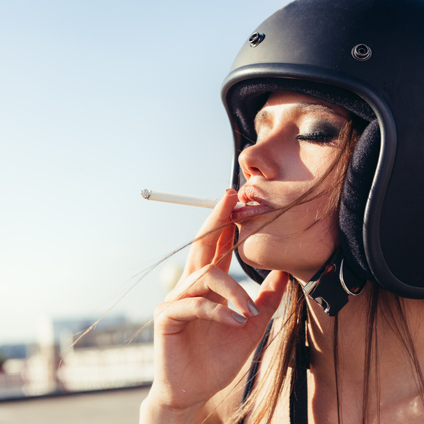 Beautiful woman in motorcycle helmet smoking sigarette - Fotó, kép