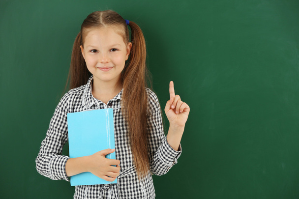 Beautiful little girl with book,  on blackboard background - Foto, Imagem