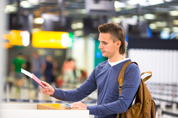 Молодий чоловік з паспортами і посадковими талонами на стійці реєстрації в аеропорту
 - Фото, зображення