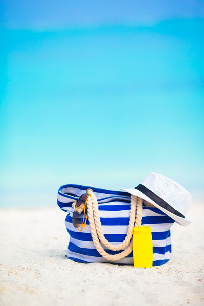Пляжні аксесуари - синя смуга сумка, солом'яний капелюх, сонцезахисні окуляри на білому пляжі
 - Фото, зображення