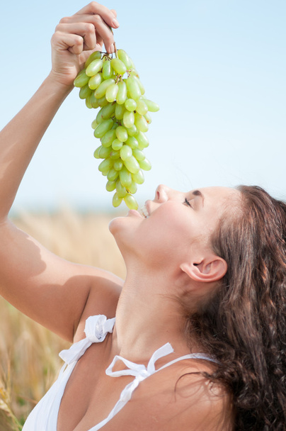 Perfect woman eating grapes in wheat field. Picnic. - Foto, Imagen