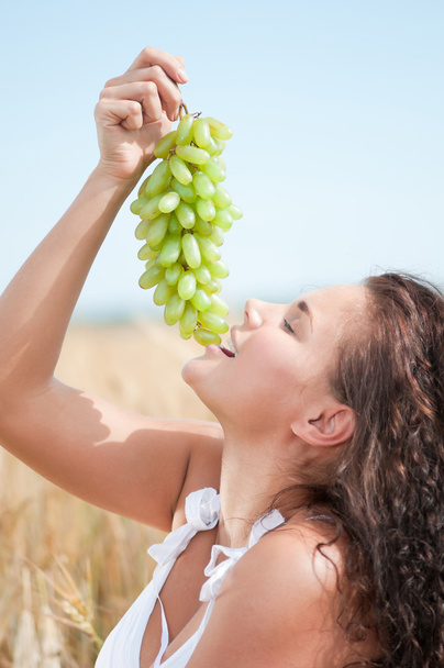 Perfect woman eating grapes in wheat field. Picnic. - Foto, afbeelding